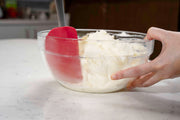 Person holding a glass bowl with a Cuisipro Red Silicone Spatula