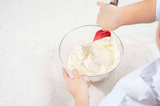 Person mixing whipped cream in a glass bowl with a Cuisipro Red Silicone Spatula