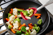 Vegetables including broccoli, cauliflower, and carrots being sautéed in a pan with a Cuisipro red Silicone Spoon with a stainless steel handle