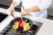 Person cooking scrambled eggs in a pan with a Cuisipro red Silicone Spoon