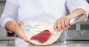 Person using a red Cuisipro spatula to blend ingredients in a glass bowl.